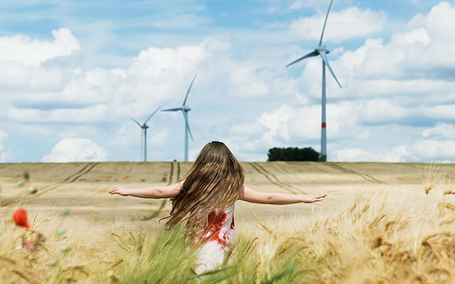 Junge Frau steht in einem Feld mit Windrädern im Hintergrund Junge Frau steht in einem Feld mit Windrädern im Hintergrund